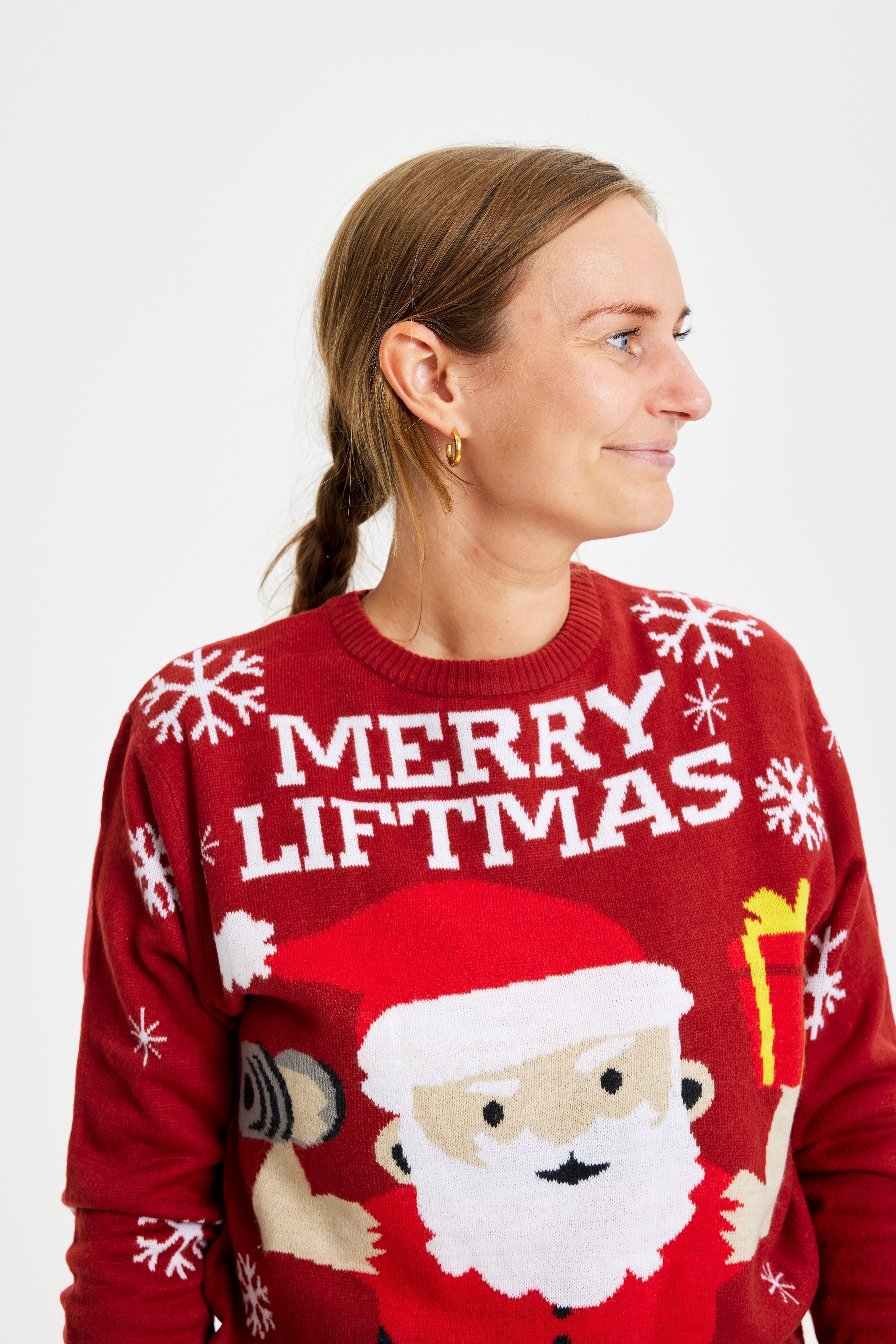 Une femme regarde de côté, vêtue d'un pull rouge de Noël avec la citation